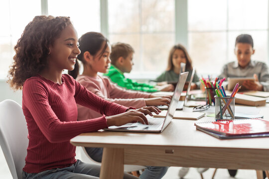 Black Schoolgirl Using Laptop Sitting With Multiethnic Classmates In Classroom