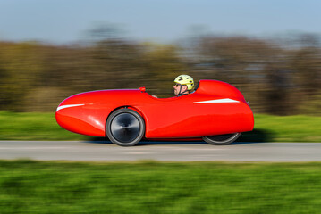A red velomobile (recumbent tricycle) rushing by on a bikepath