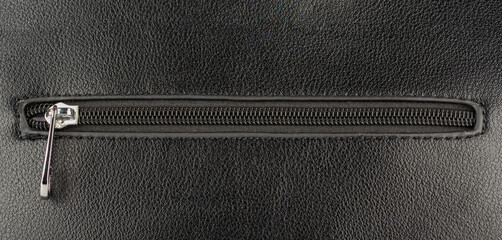 Closed zip fastening on black leather surface. © svdolgov