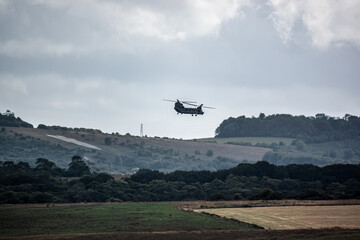 RAF Chinook tandem-rotor CH-47 helicopter flying fast and low in a cloudy blue grey sky on a military battle exercise, Wilts UK - obrazy, fototapety, plakaty