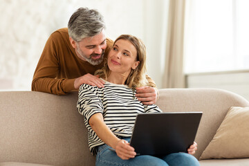 Happy Middle Aged Couple Using Laptop Computer At Home