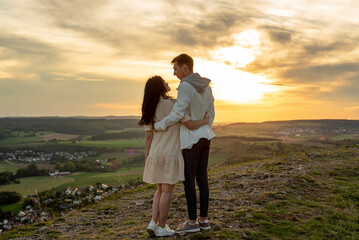 A couple in love stands on a mountain at sunset