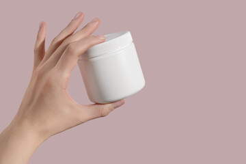 Hand holding blank white plastic supplement container on pink background. Package mockup blank for capsule.