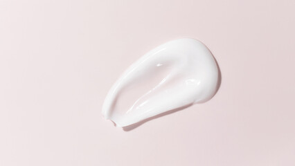 White beauty cream smear smudge on pink background. Cosmetic skincare product texture. Face cream, body lotion swipe swatch