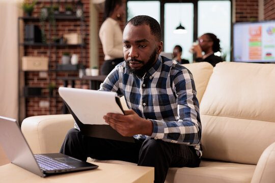 Corporate worker analyzing documents in office, doing paperwork with data and information for research. Creating business report on papers to send email to manager, using laptop.