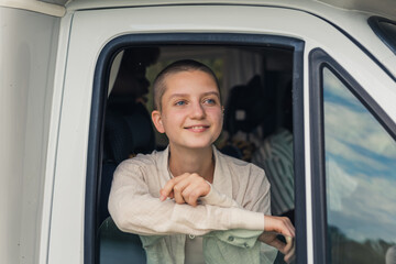 Young caucasian beautiful girl with shaved head looking out of the open window of a camping van in awe, marveling over the beautiful scenery. High quality photo