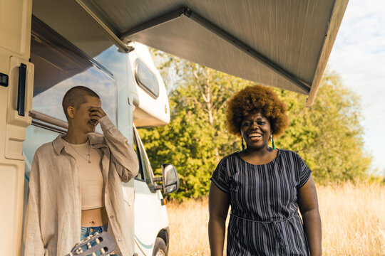 Close interracial friendship. Delighted happy mixed race girls laughing at a joke and having fun during their weekend spent in nature with a camping van. High quality photo