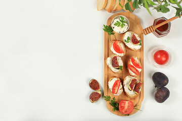 Healthy breakfast with ingredients, toast with figs, tomatoes and soft cream cheese and honey, Canape or crostini with fried baguette and herbs on a light sunny table, italian recipes menu, 