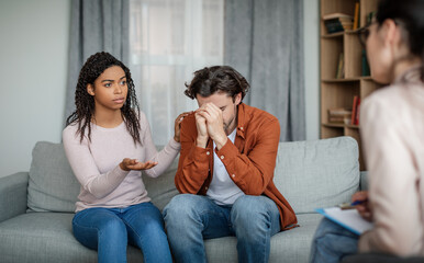 Sad black wife calms depressive european husband on consultation with psychologist, couple need professional help