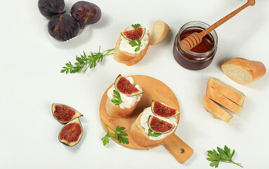 Healthy breakfast with ingredients, toast with figs and soft cream cheese and honey, Canape or crostini with fried baguette and herbs on a light sunny table, italian recipes menu, selective focus