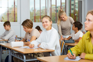 Teenage girl looking at camera while sitting at desk in classroom and studying.