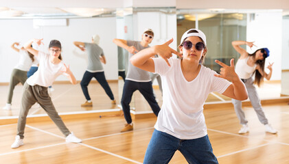 Plakat Group of teenagers in casual clothes training hip-hop in class, learning modern dance movements