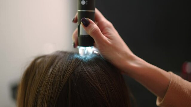 Side view close-up trichoscope in female Caucasian hand in hair salon. Unrecognizable expert examining hair of client in beauty parlor indoors