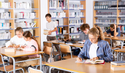 Obraz na płótnie Canvas Teenage boys and girls reading books and doing homework in library.