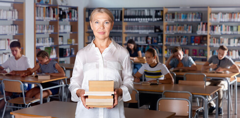 Portrait of friendly smiling mature woman teacher standing in classroom