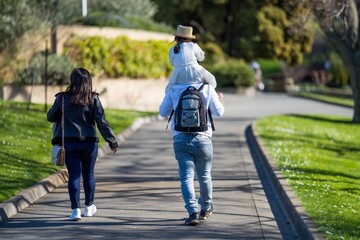 family with daughter on her dads shoulders in a park in spring 