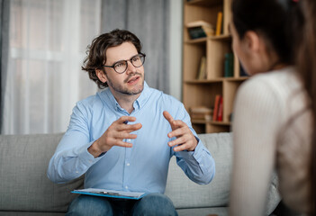 Emotional young european guy doctor speaks and gesticulates with woman patient in office clinic interior