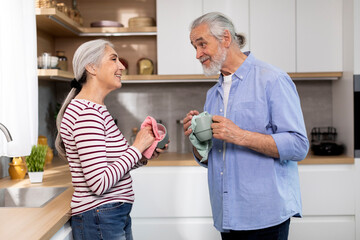 Fototapeta premium Happy Senior Spouses Sharing Domestic Chores, Wiping Dishes Together In Kitchen