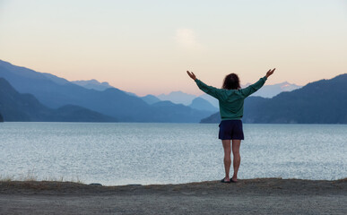 Fototapeta na wymiar Adventure Woman looking at Harrison Lake during Sunny Summer Morning Sunrise. Canadian Nature Landscape Background. Harrison Hot Springs, British Columbia, Canada. Travel Concept