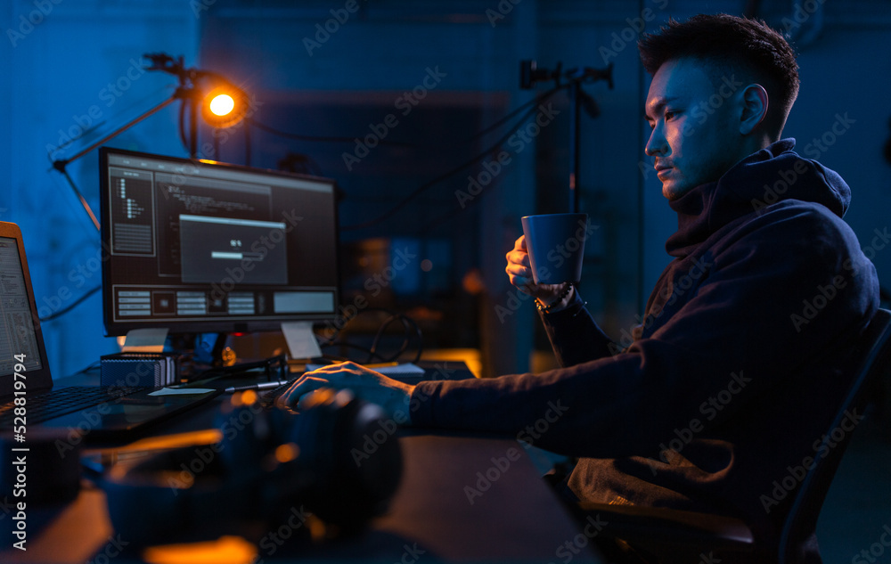 Poster cybercrime, hacking and technology concept - male hacker in dark room drinking coffee and using comp