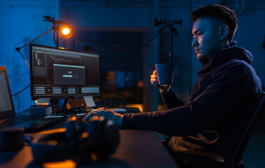 cybercrime, hacking and technology concept - male hacker in dark room drinking coffee and using...