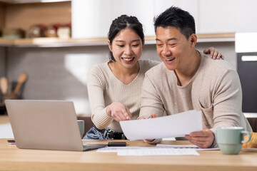Cheerful asian spouses paying bills on Internet, using laptop