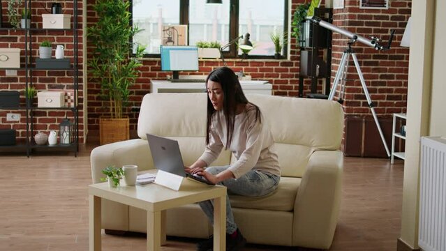 Hurried asian woman working remotely on startup project because of early deadline. Beautiful freelancer doing remote work on modern laptop while developing business ideas at home.