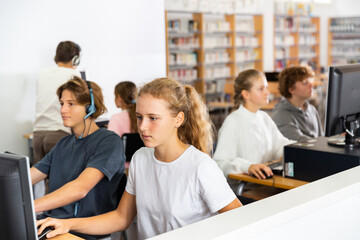 Obraz premium Portrait of a fifteen-year-old schoolgirl studying at a computer in a class at an informatics lesson with classmates