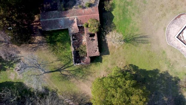 Looking down on dilapidated building with fallen in red tile roof trees growing in buildings big green trees all around building