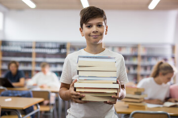 Teenager boy standing with a stack of books in the library