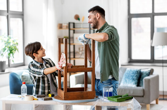 renovation, diy and home improvement concept - happy smiling father and son degreasing old round wooden table surface with tissue