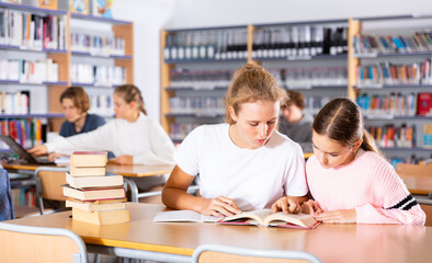 Two female friends reading books together and preparing for exams in the school library