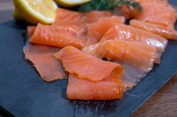 Slices of tasty smoked Scottish salmon fish served on black plate with lemon and fresh dill
