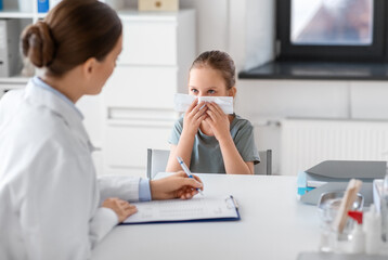 medicine, healthcare and pediatry concept - female doctor or pediatrician and little girl patient blowing her nose on medical exam at clinic