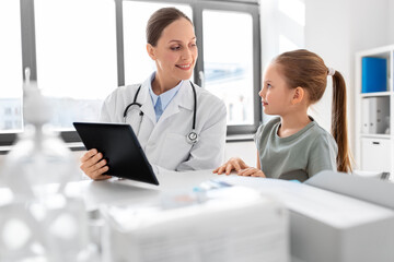 medicine, healthcare, pediatry and people concept - female doctor or pediatrician showing tablet computer to little girl patient at clinic
