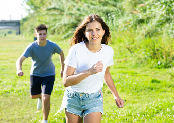 Young man and girl are running on the grass together