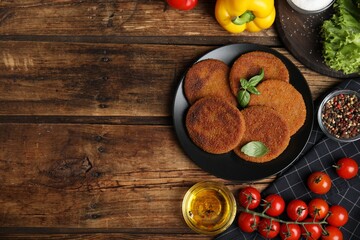 Delicious fried breaded cutlets, spices and vegetables on wooden table, flat lay. Space for text