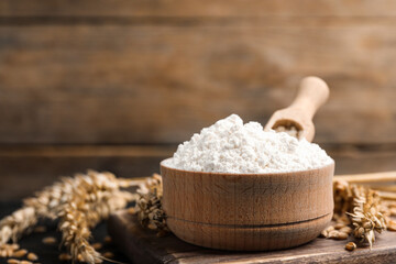 Wheat flour in bowl, spikes and grains on wooden board, closeup. Space for text