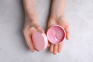 Woman holding package of under eye patches at light table, top view. Cosmetic product