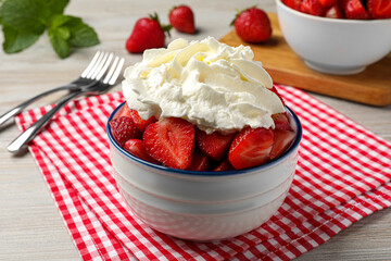 Bowl with delicious strawberries and whipped cream served on wooden table