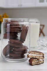 Jar with delicious choco pies and glass of milk on white table in kitchen