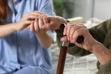 Caregiver and elderly woman with walking cane at home, closeup