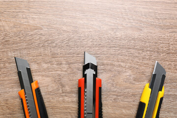 Three different utility knives on wooden table, flat lay. Space for text