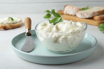 Tasty cream cheese with basil and knife on white wooden table