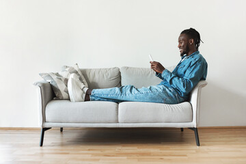 Fototapeta na wymiar Cheerful Black Man Using Mobile Phone Texting Sitting At Home