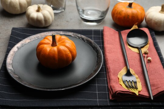 Seasonal table setting with pumpkins and autumn leaves on grey background