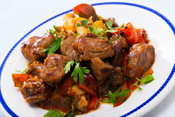 Cooked fried pork meat with peppers, mushrooms and greens on plate