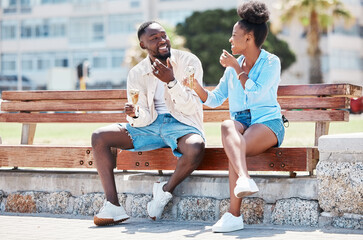 Happy black couple eating ice cream on a beach bench together, smiling while bonding and laughing. Young African American man and woman enjoying their summer romance, free time and relationship