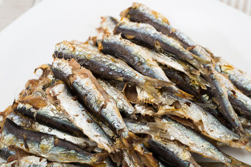 Image of deliciously cooked baked sprats served on white plate at table - obrazy, fototapety, plakaty