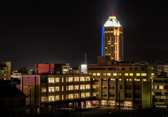 High rise building towers over lit multi-story school at night - 528825174